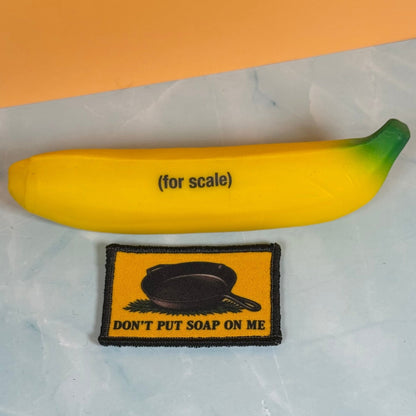 Iron Skillet Gadsden, Don't Put Soap On Me patch in yellow with a black skillet silhouette and lettering, beside a yellow banana-shaped object
