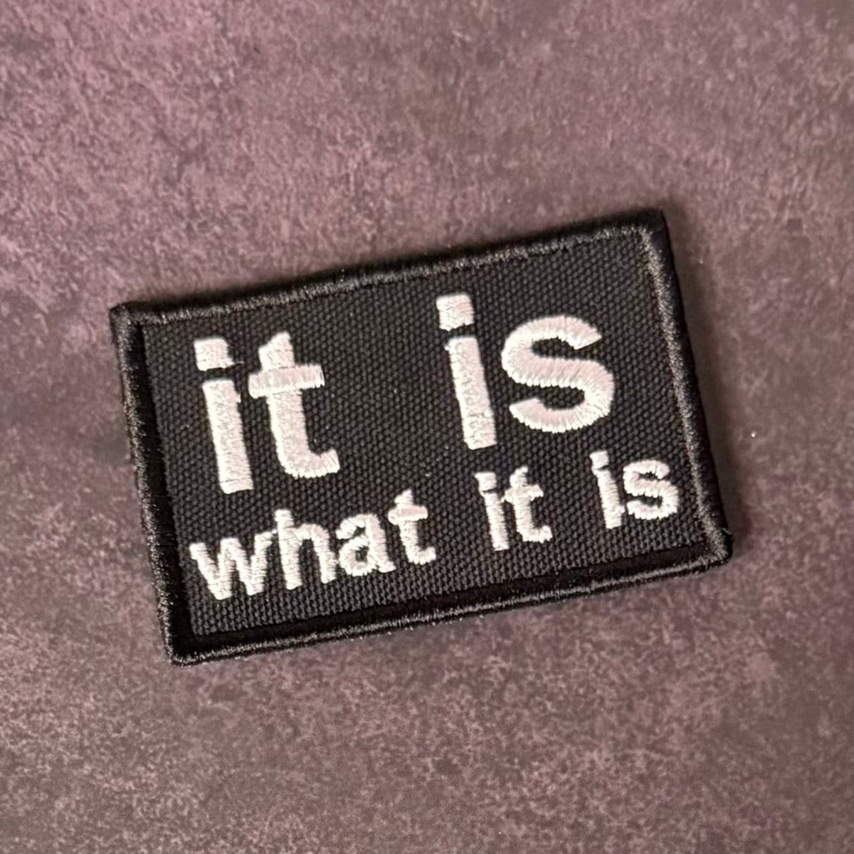Front view of It Is What It Is patch in black with white lowercase lettering