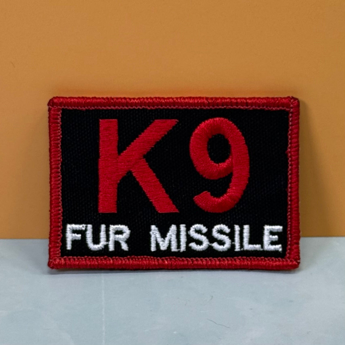 Front view of K-9 Fur Missile patch in black with red K9 and border and white FUR MISSILE lettering