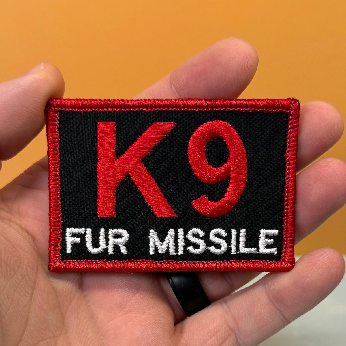K-9 Fur Missile patch in black with red K9 and border and white FUR MISSILE lettering, held in a hand