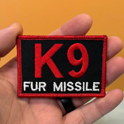 K-9 Fur Missile patch in black with red K9 and border and white FUR MISSILE lettering, held in a hand