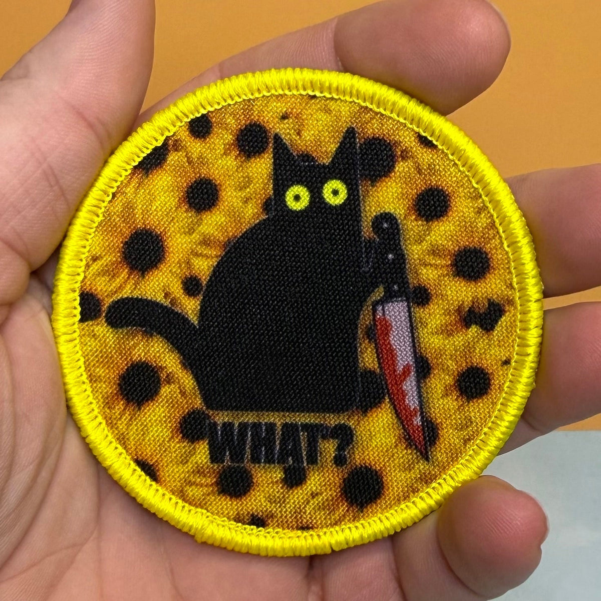 Murder Cat & Sunflowers patch in yellow with a black cat, sunflowers and a red knife, held in a hand