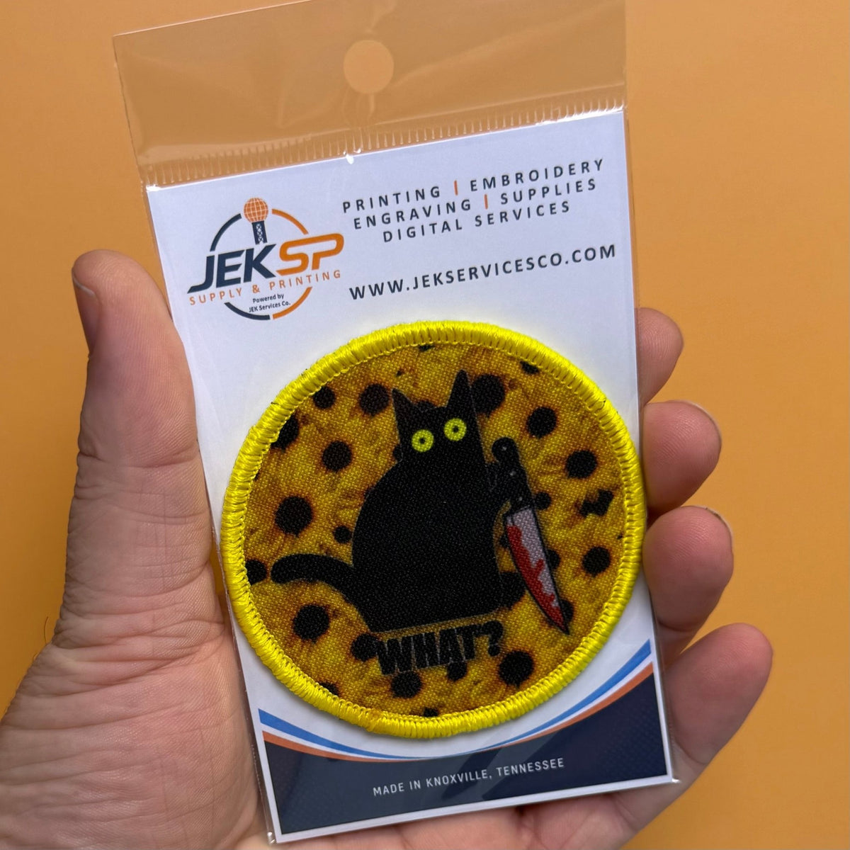 Murder Cat & Sunflowers patch in yellow with a black cat, sunflowers and a red knife, retail package held in a hand