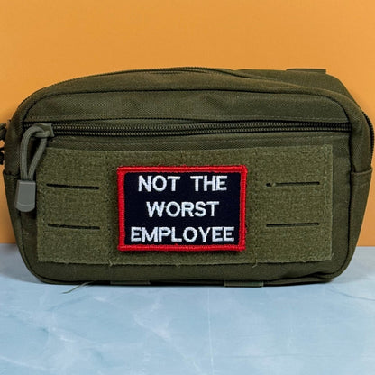 Not The Worst Employee patch in black with white lettering and a red border, mounted on an olive utility pouch
