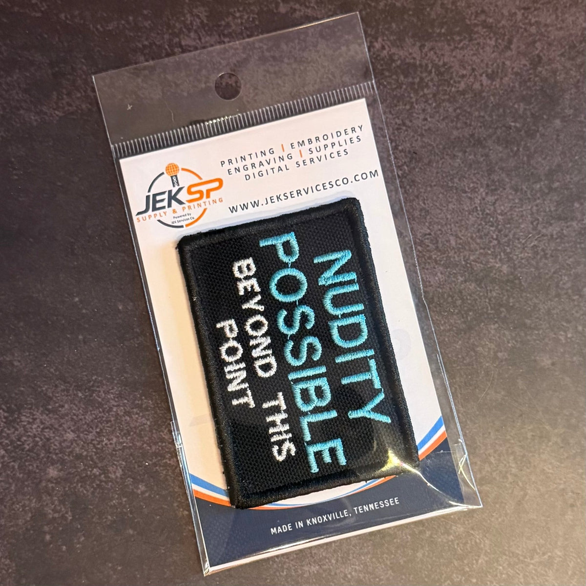 Nude Beach Warning patch in black with blue NUDITY POSSIBLE and white lettering, in clear retail packaging