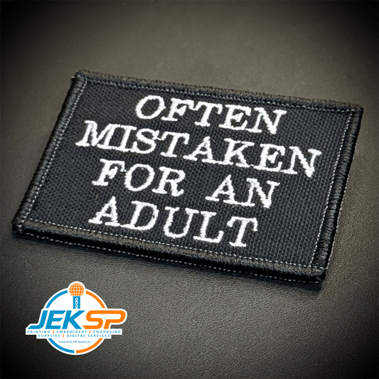 Front view of Often Mistaken For An Adult patch in black with white lettering