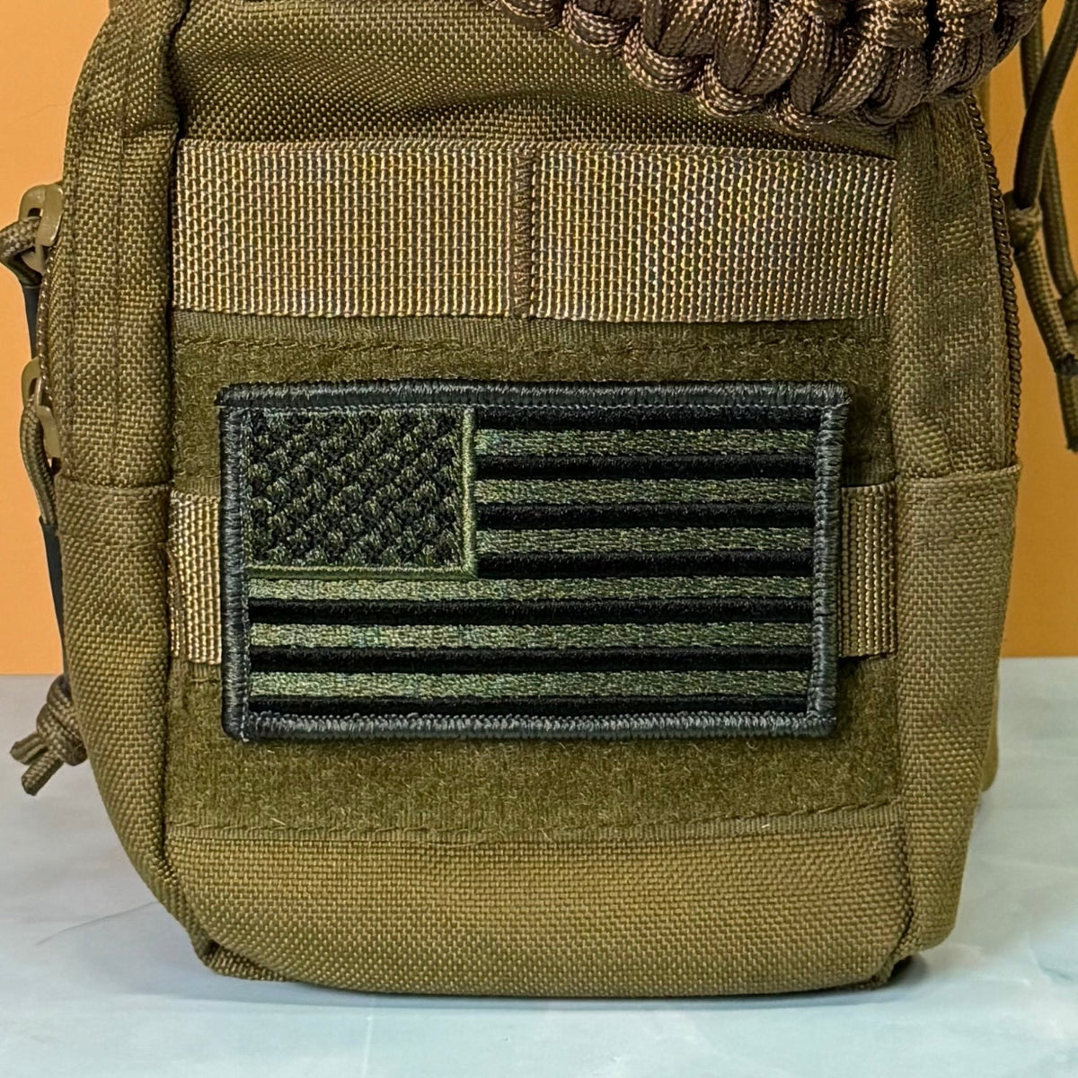 Olive OD Green Tactical American Flag patch in olive green and black stars and stripes, mounted on an olive backpack