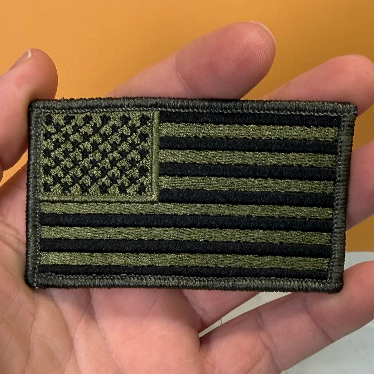 Olive OD Green Tactical American Flag patch in olive green and black stars and stripes, held in a hand