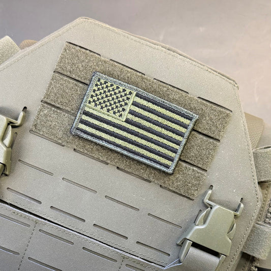 Olive OD Green Tactical American Flag patch in olive green and black stars and stripes, mounted on a tan plate carrier