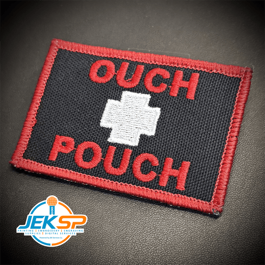 Front view of Ouch Pouch patch in black with red lettering and border and a white medical cross