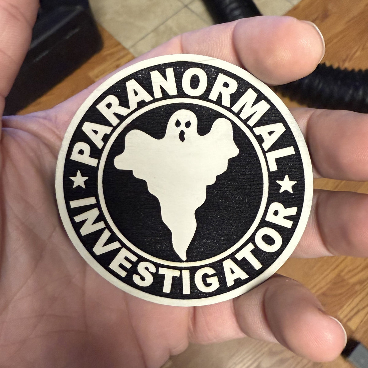 Paranormal Investigator patch in black and white with a ghost silhouette, stars and circular lettering, held in a hand