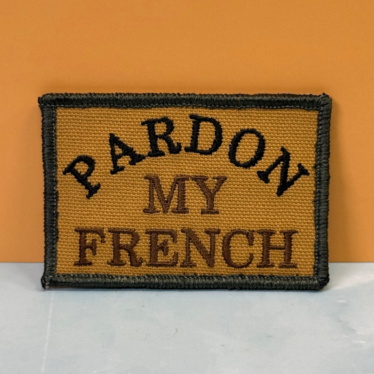 Front view of Pardon My French patch in tan with black lettering and border
