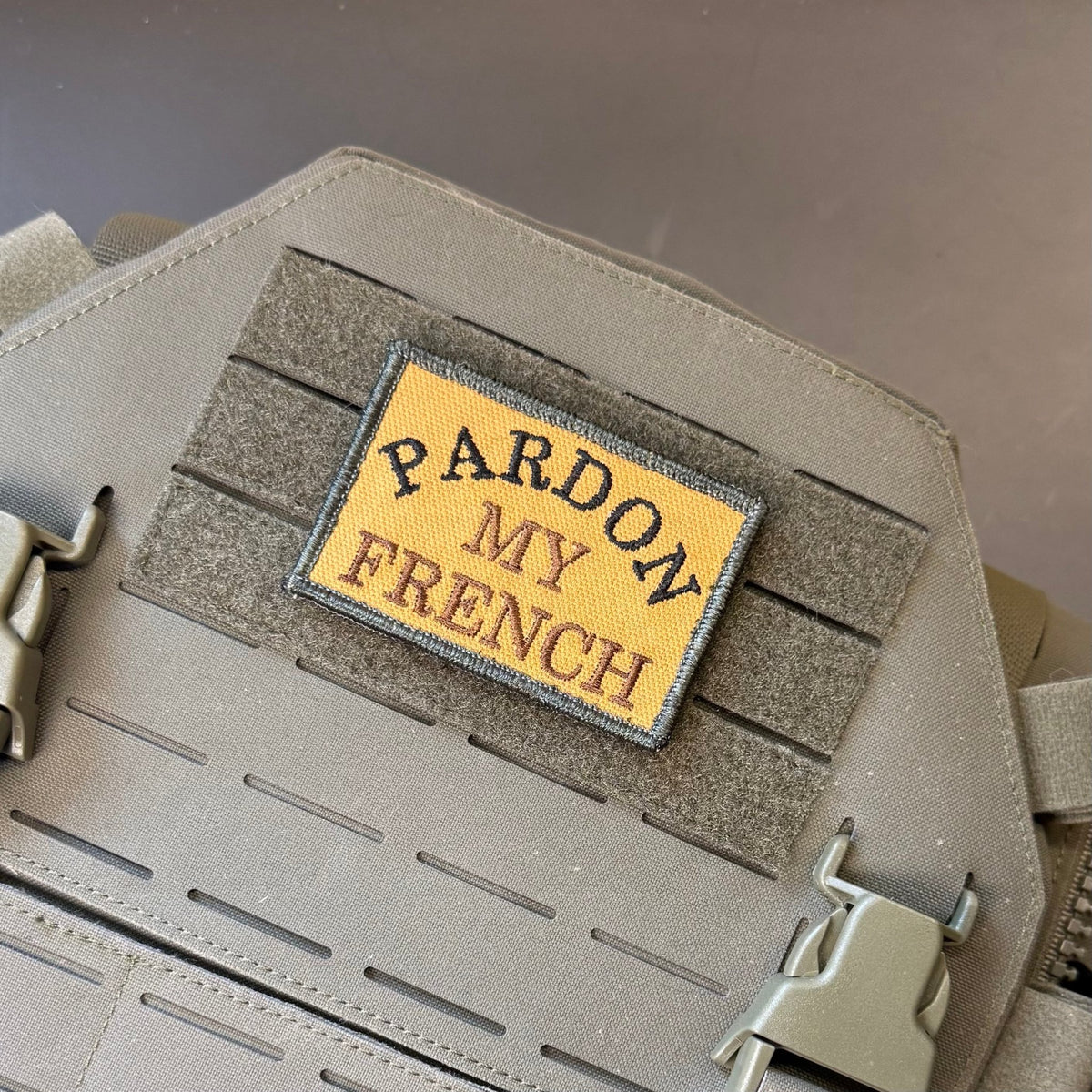 Pardon My French patch in tan with black lettering and border, mounted on a tan plate carrier