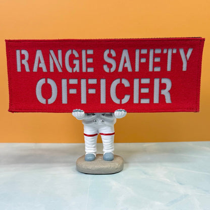 Range Safety Officer Patches & ID Panels patch in red with white Range Safety Officer lettering, propped on a small astronaut figurine