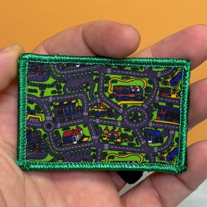 Retro Toy Car Rug Carpet patch in multicolored toy-road-map design with a green border, held in a hand