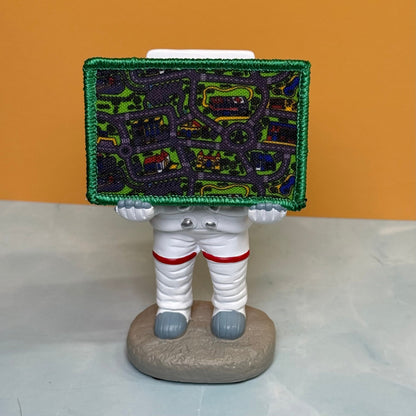 Retro Toy Car Rug Carpet patch in multicolored toy-road-map design with a green border, propped on a small astronaut figurine