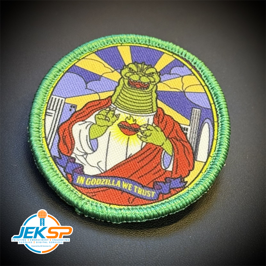 Front view of Saint Zilla, In Godzilla We Trust patch in green-bordered oval with a robed green monster and purple-yellow stained-glass background