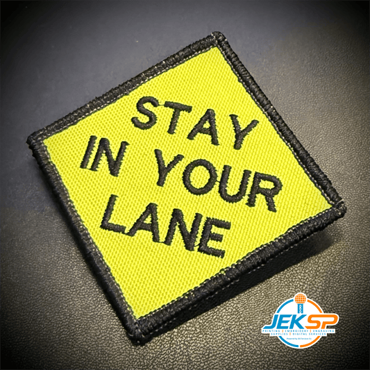 Front view of Stay In Your Lane patch in yellow diamond with black lettering and border