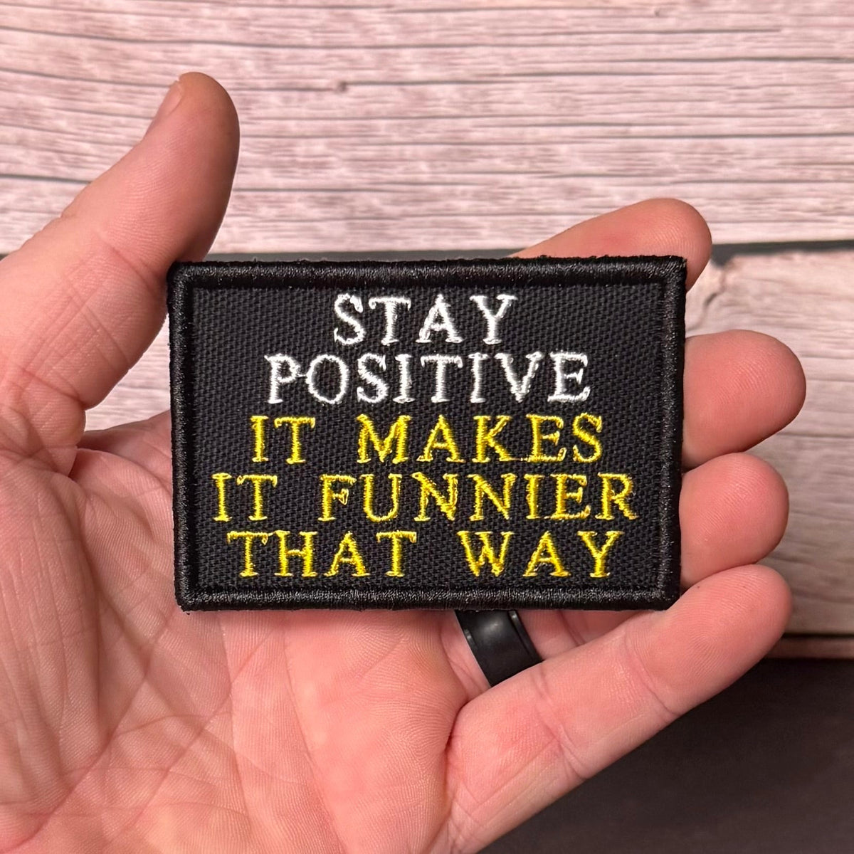 Stay Positive patch in black with white and yellow lettering, held in a hand