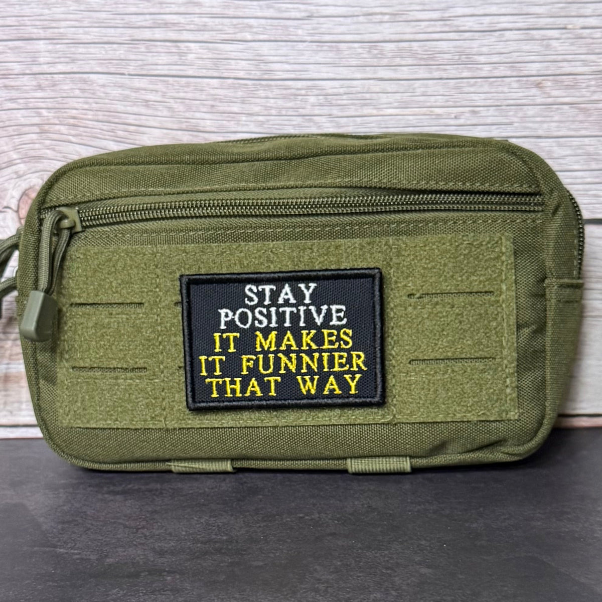 Stay Positive patch in black with white and yellow lettering, mounted on an olive utility pouch