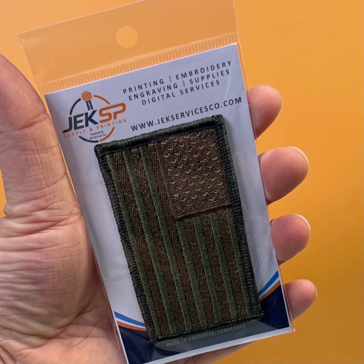 Subdued FDE Tactical American Flag patch in subdued tan and green American flag, retail package held in a hand