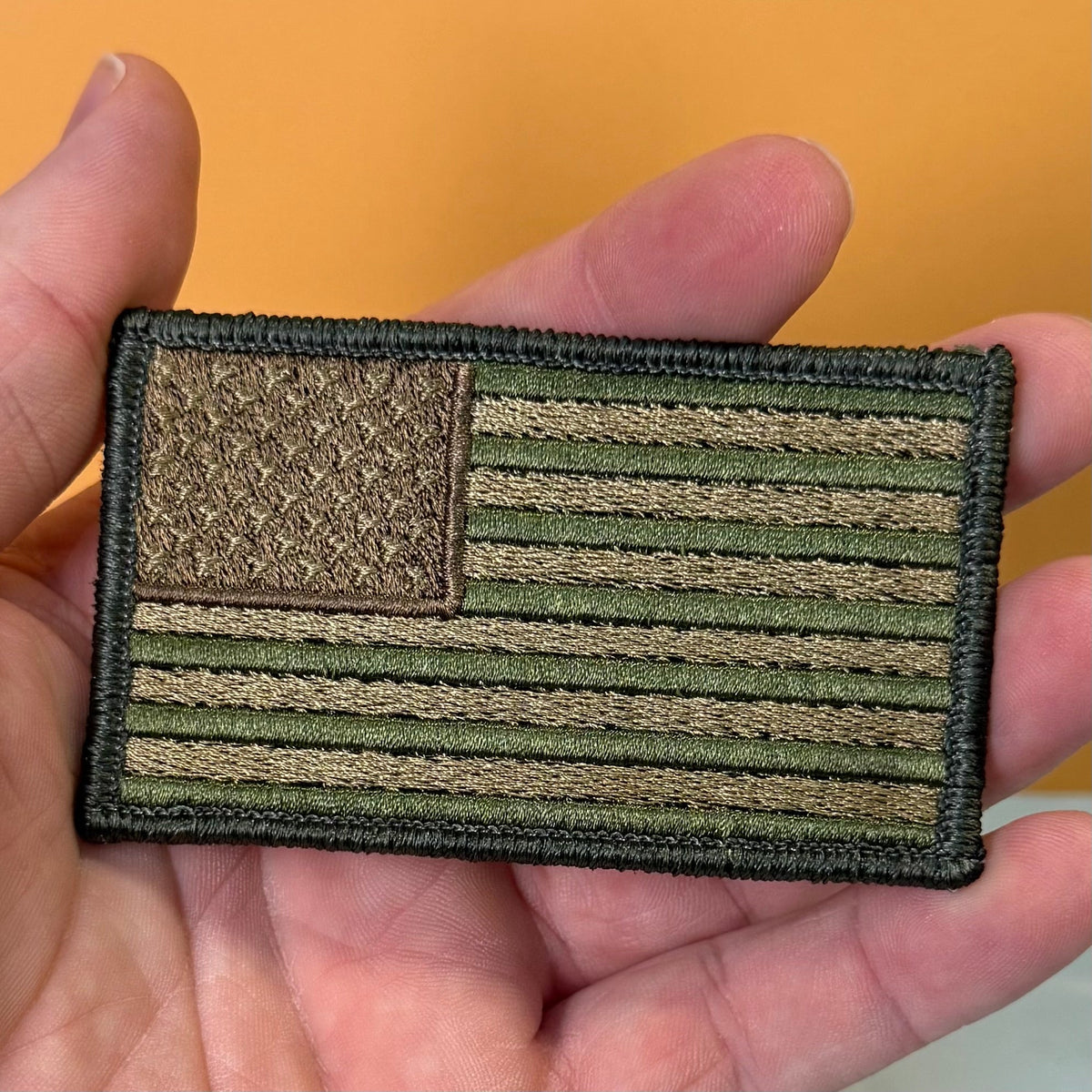 Subdued FDE Tactical American Flag patch in subdued tan and green American flag, held in a hand