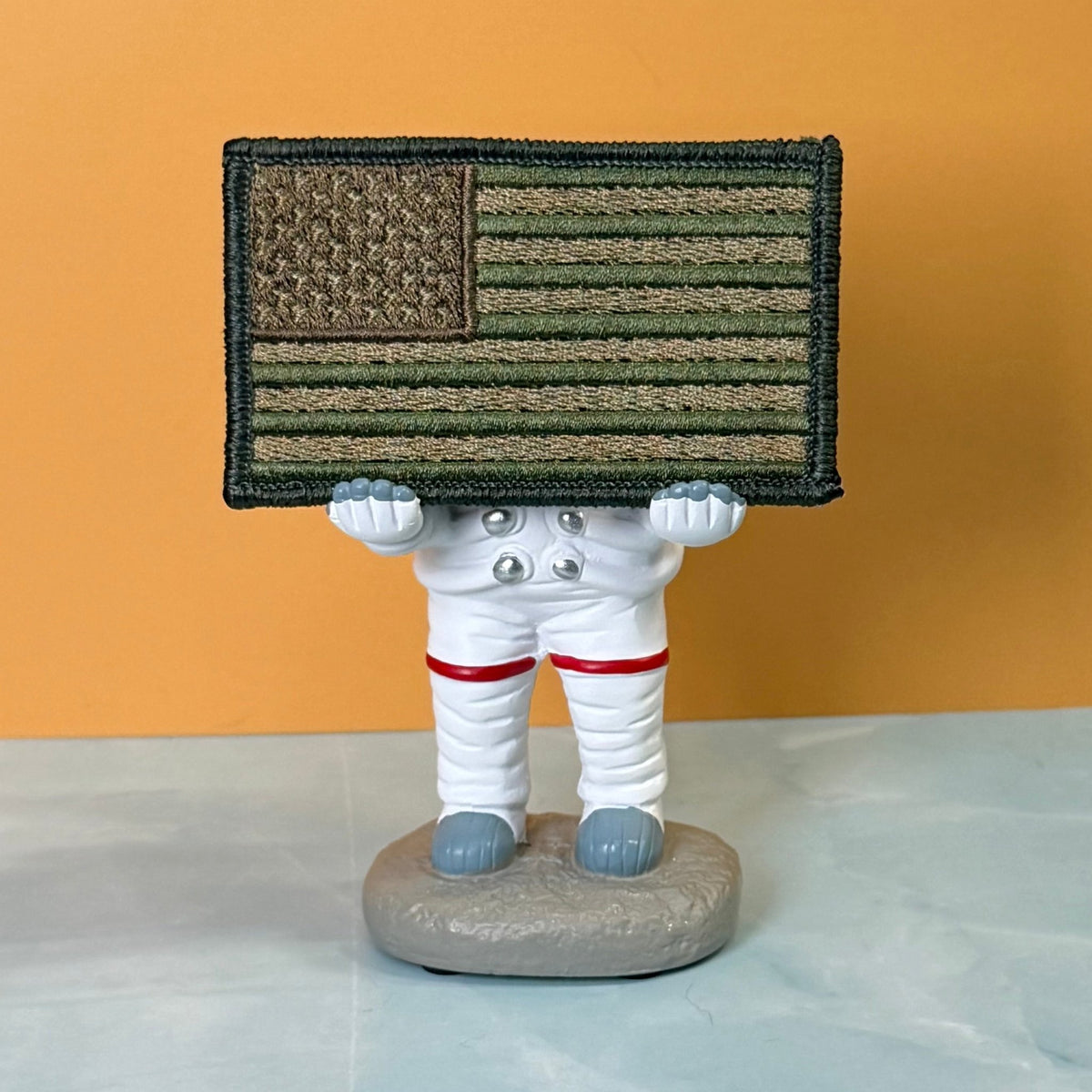 Subdued FDE Tactical American Flag patch in subdued tan and green American flag, propped on a small astronaut figurine