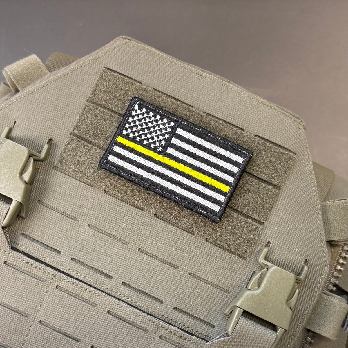 Thin Yellow Line American Flag patch in black and white American flag with one yellow stripe, mounted on a tan plate carrier