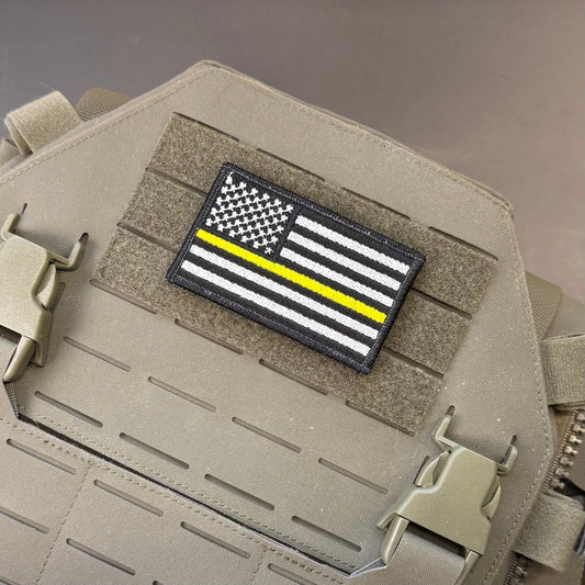 Thin Yellow Line American Flag patch in black and white American flag with one yellow stripe, mounted on a tan plate carrier