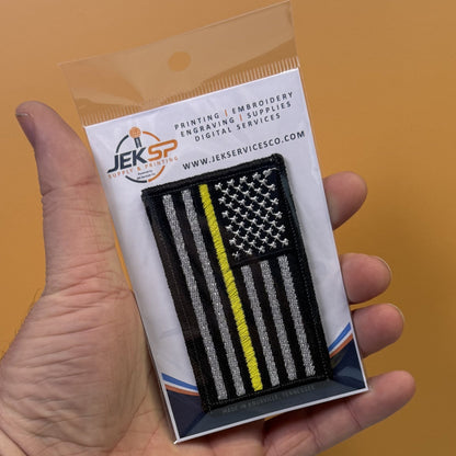 Thin Yellow Line American Flag patch in black and white American flag with one yellow stripe, retail package held in a hand