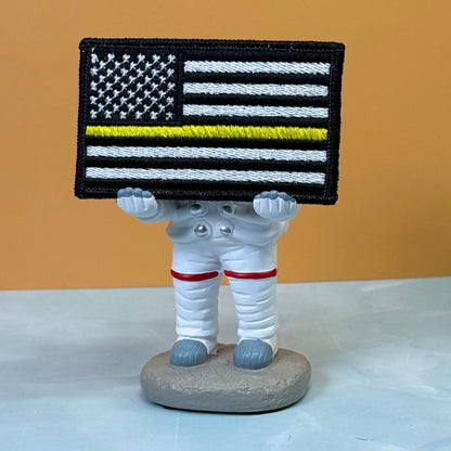 Thin Yellow Line American Flag patch in black and white American flag with one yellow stripe, propped on a small astronaut figurine