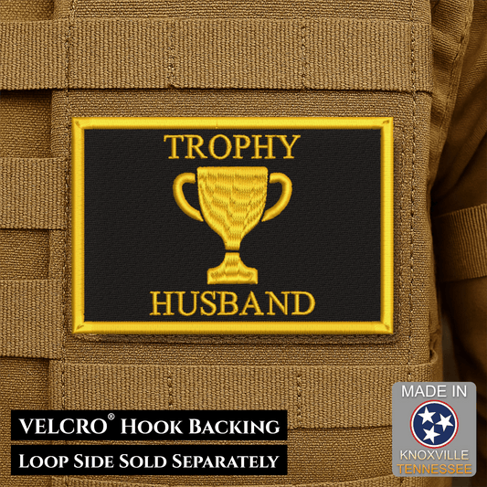 Front design and hook backing of Trophy Husband patch in black with a yellow trophy, lettering and border