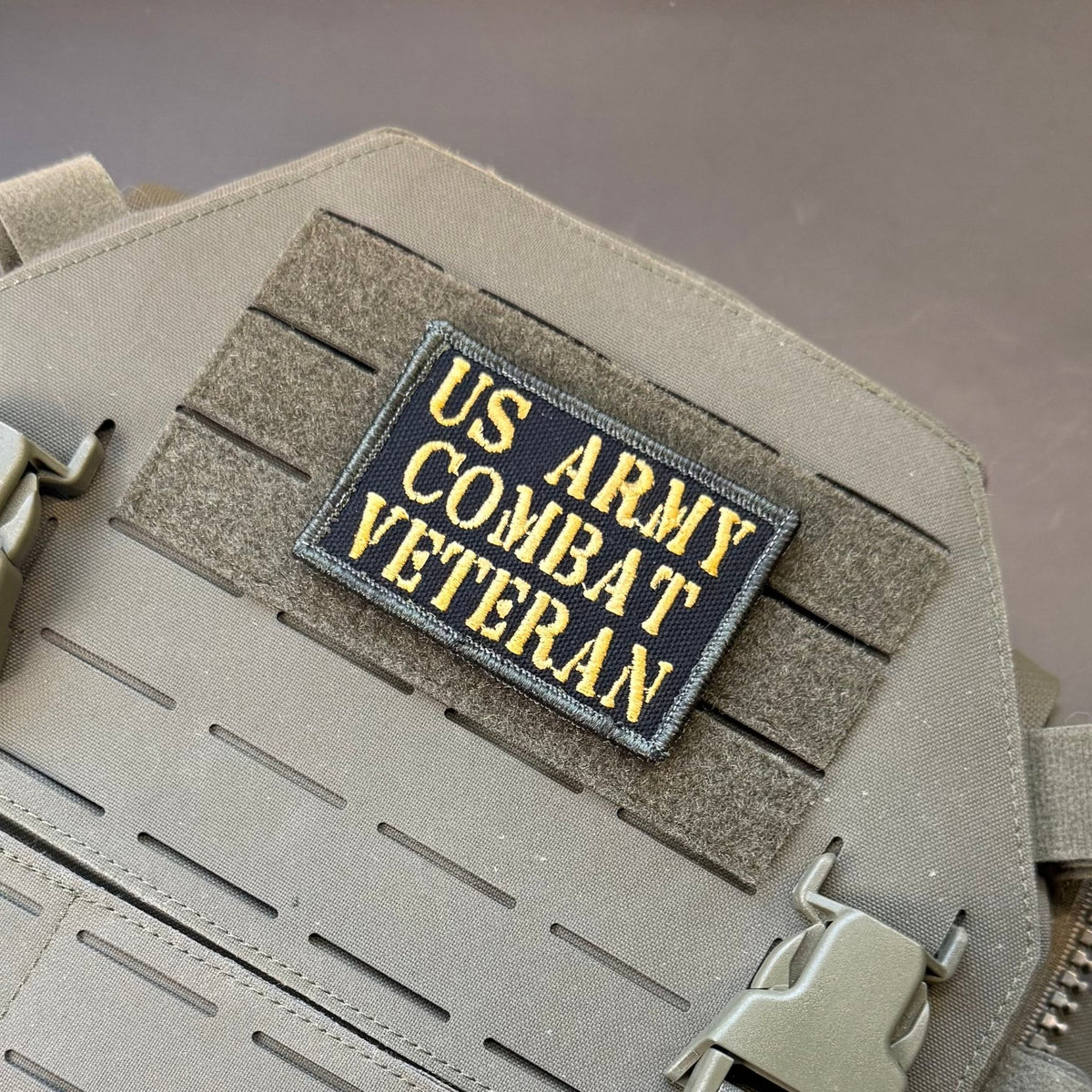 US Army Combat Veteran patch in black with tan lettering, mounted on a tan plate carrier