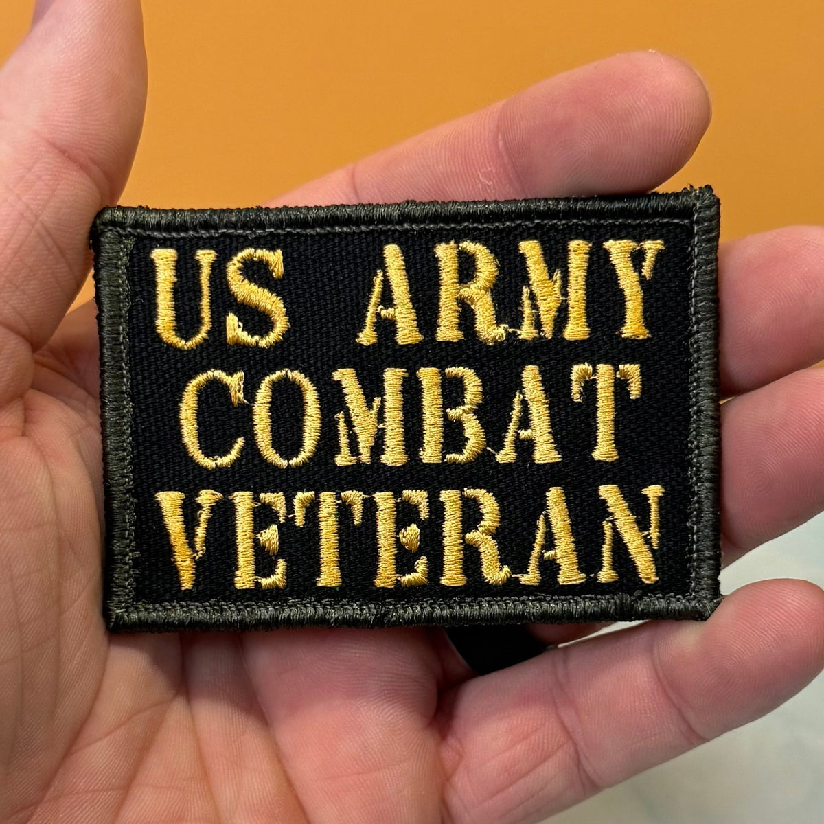 US Army Combat Veteran patch in black with tan lettering, held in a hand