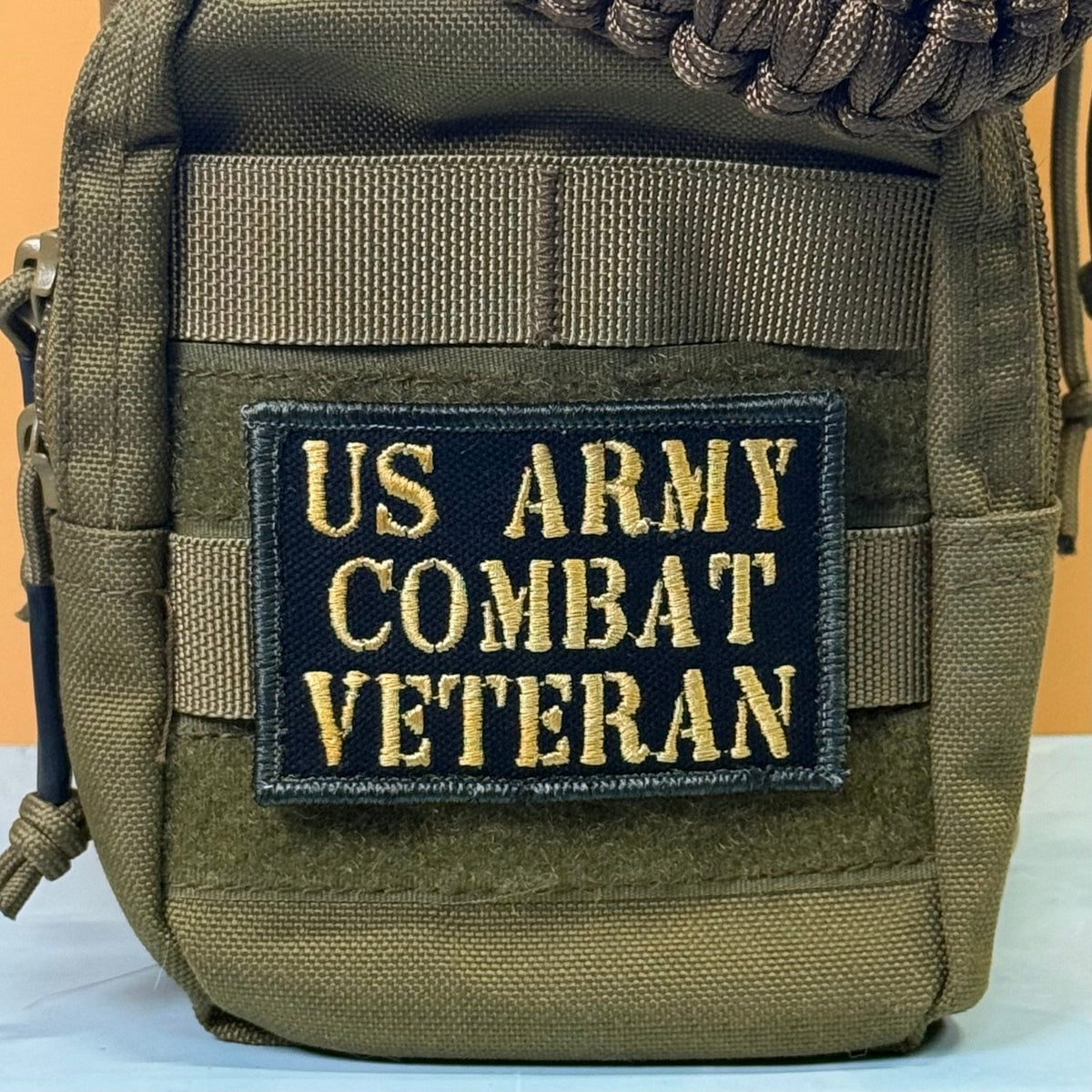 US Army Combat Veteran patch in black with tan lettering, mounted on an olive backpack
