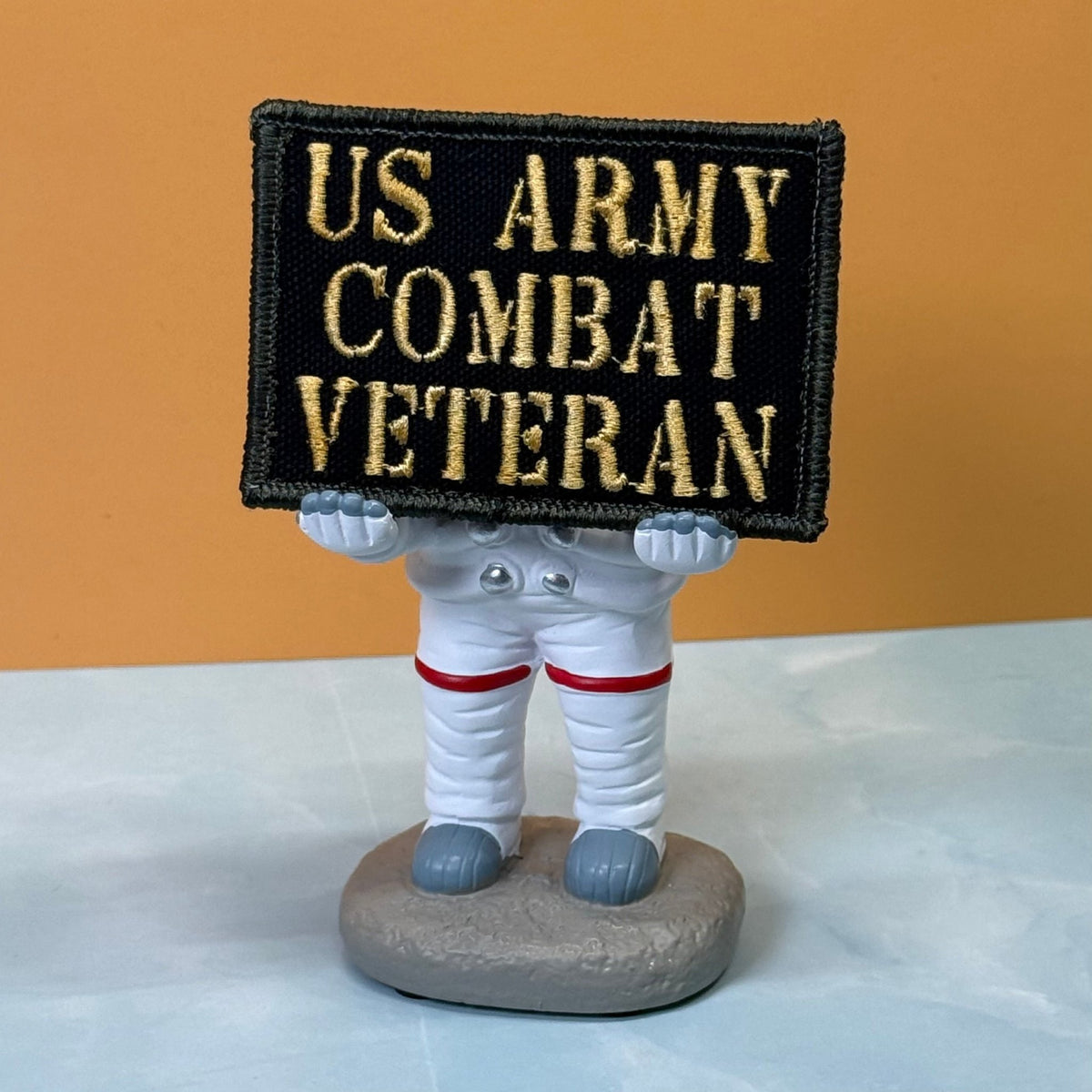 US Army Combat Veteran patch in black with tan lettering, propped on a small astronaut figurine