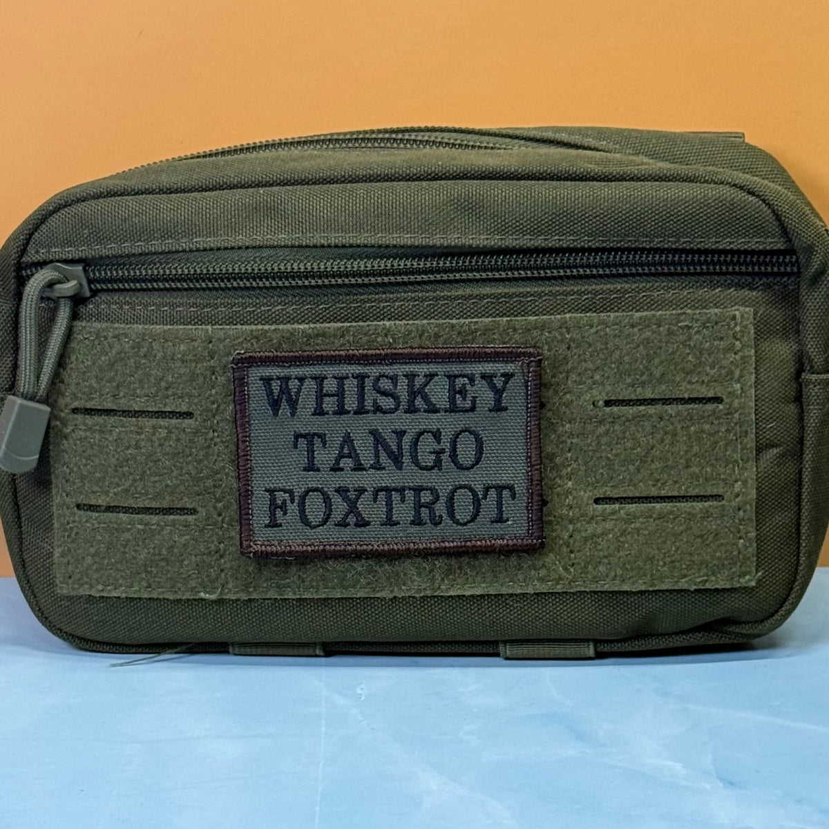 Whiskey Tango Foxtrot WTF patch in olive green with black lettering, mounted on an olive utility pouch