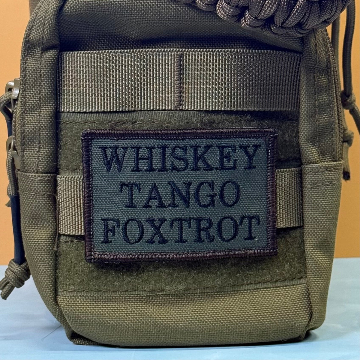Whiskey Tango Foxtrot WTF patch in olive green with black lettering, mounted on an olive backpack