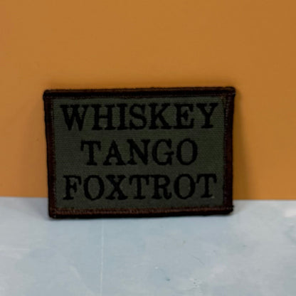 Front view of Whiskey Tango Foxtrot WTF patch in olive green with black lettering