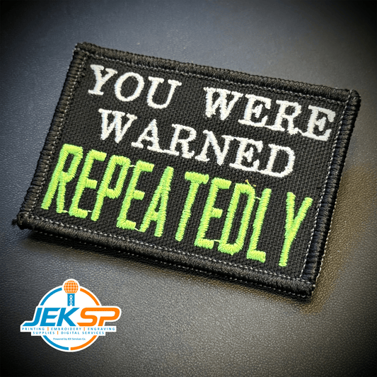Front view of You Were Warned, Repeatedly patch in black with white lettering and bright green REPEATEDLY text