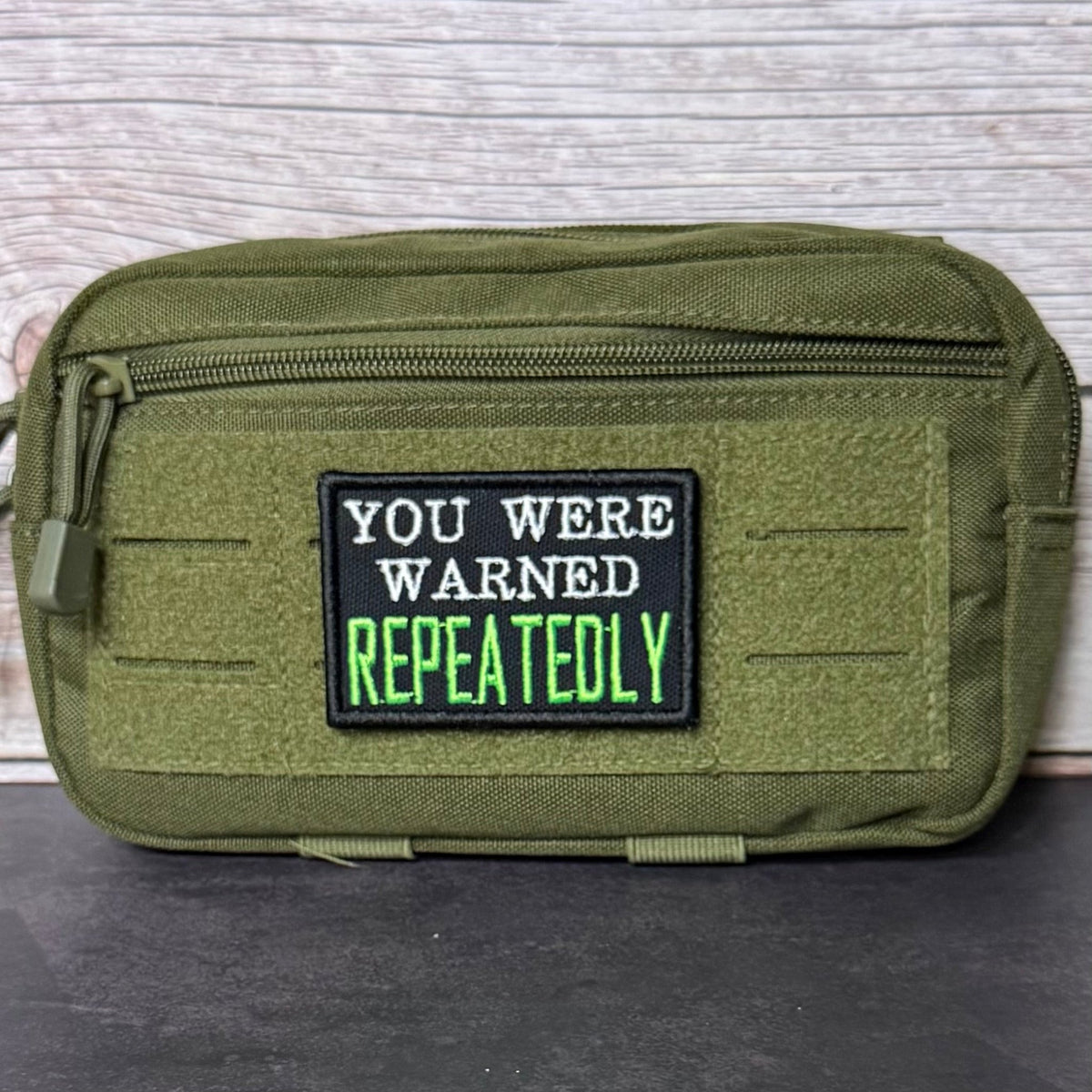 You Were Warned, Repeatedly patch in black with white lettering and bright green REPEATEDLY text, mounted on an olive utility pouch